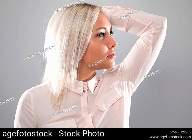 Beautiful female model holding her blonde hair and wearing a shirt. Serious looking with large eyes