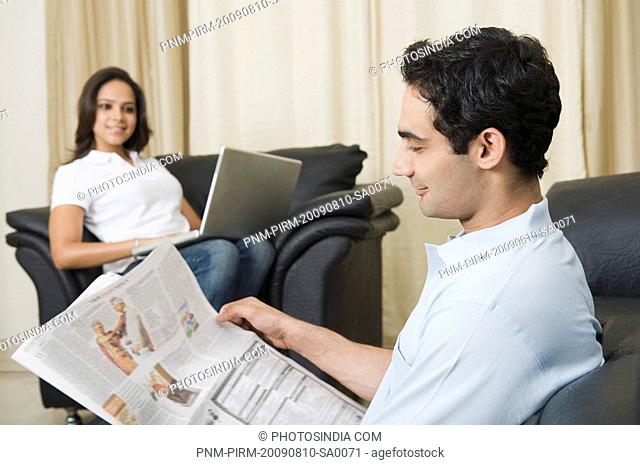 Man reading a newspaper with his wife using a laptop