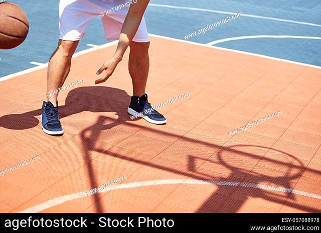 young asian adult playing basketball under summer sun on outdoor court