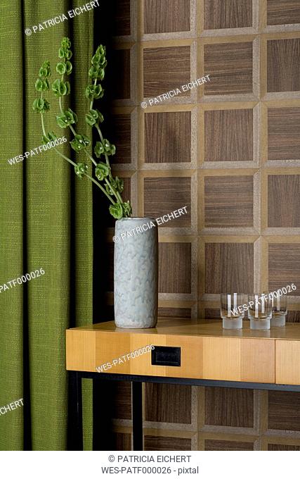 Sideboard with glasses and flower vase in front of wooden wall cladding