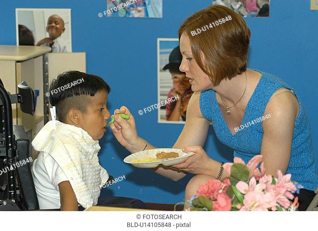 Little boy with multiple disabilities, including the ability to feed himself, receiving assistance in eating from a care provider