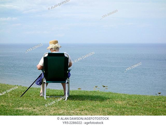 Elderly woman reading book overlooking sea at Whitby, North Yorkshire, England, UK