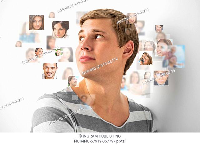 Young man standing and smiling with many different people's faces around him. Technology social media network of friends and communication