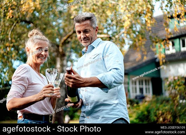 Couple holding champagne flutes and bottle at backyard