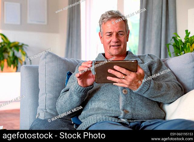 Happy caucasian senior man sitting on sofa and using tablet