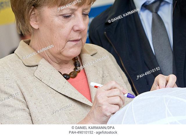 German Federal Chancellor Angela Merkel (CDU) visits the booth of the catholic association for girls and women's social service work 'In Via' and writes down...