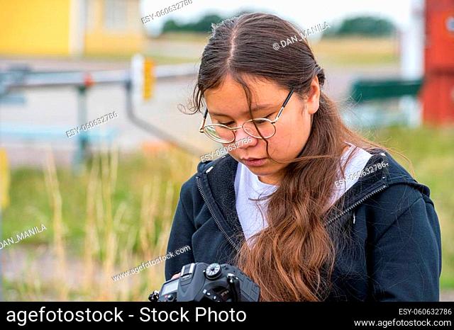 A young preteen girl takes photos with a DSLR Camera. She looks straight into the camera. Blurry, soft background