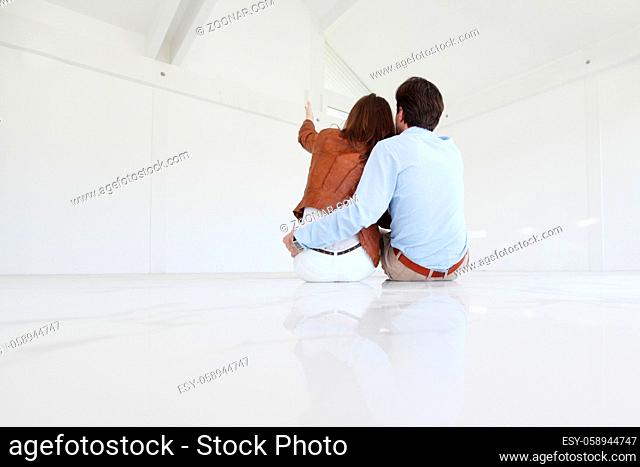Couple at their new empty apartment pointing at space and planning future