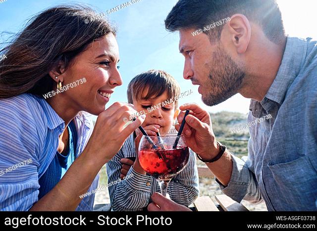Happy father and mother with son drinking juice on sunny day