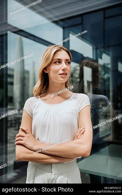 Young woman with arms crossed looking away in front of glass wall