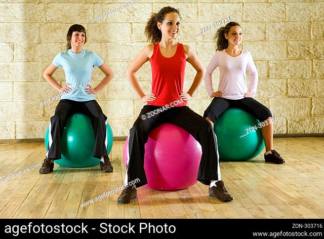A group of women making exercise sitting on big balls and holding hands on hips. Front view