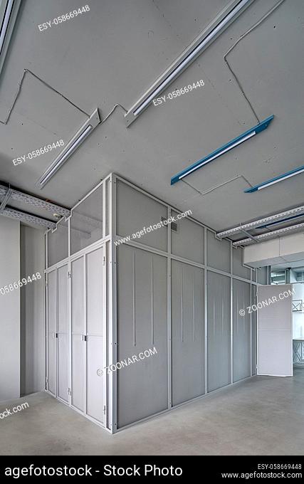 Room with the gray mesh metal walls and doors in the business interior in a loft style. On the ceiling there are lamps and communications. Vertical