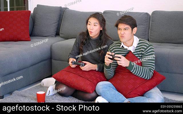 Happy Asian beautiful young family couple husband and wife smile and laugh enjoying funny with each other playing video game, holding joysticks console