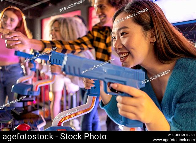 Happy young woman enjoying shooting game with friends at arcade