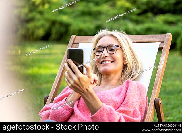Smiling mature woman using smartphone while sitting on deckchair