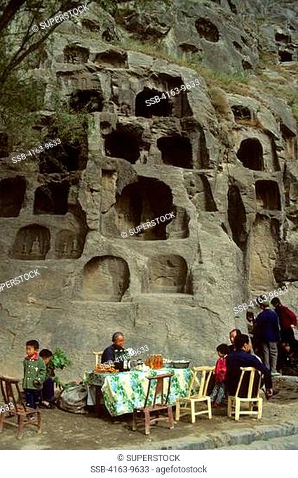 CHINA, LUOYANG LONGMEN GROTTOES, BUDDHIST STATUES CARVED INTO ROCK CLIFFS, PEOPLE SELLING SNACKS