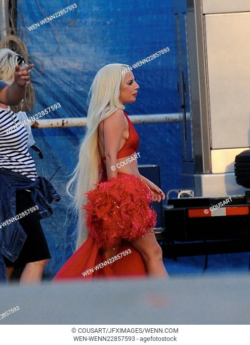Lady Gaga leaves little to the imagination as she steps out of her trailer in a red dress with a long slit that showed off her toned legs for a scene in...