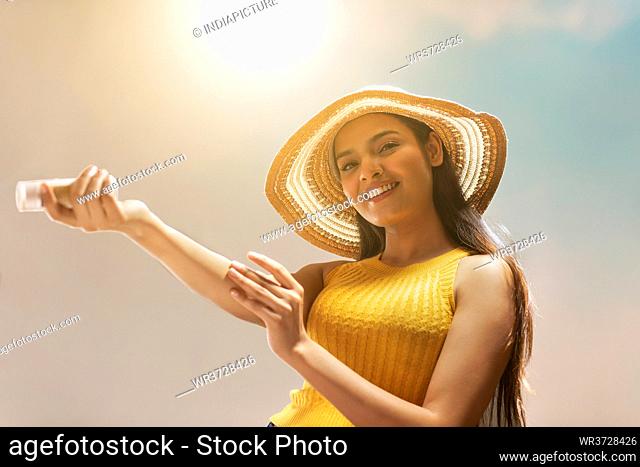 A YOUNG WOMAN LOOKING AT CAMERA AND HAPPILY APPLYING MOISTURIZER