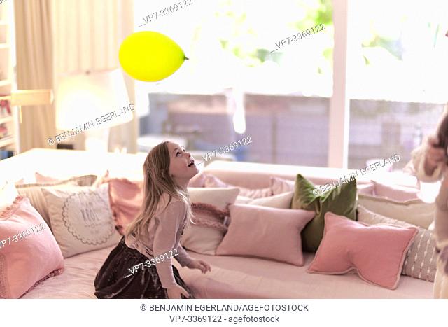 little girl playing header with party balloon in living room