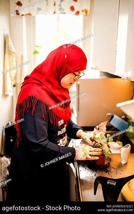 Woman in kitchen potting plant