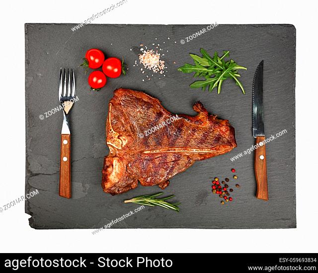 Close up one big grill roasted T-bone porterhouse beef steak with rib bone served on black slate cutting board isolated on white background, elevated top view