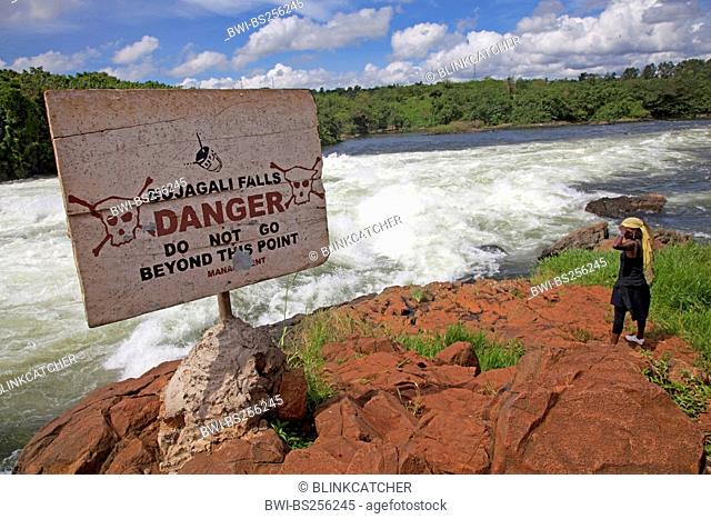 Female tourist standing at the Bujagali waterfalls, danger sign hinting at dangerous water, Uganda, Jinja