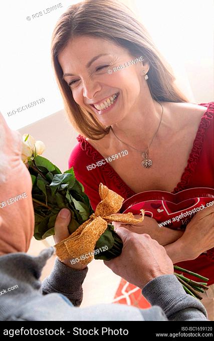 Senior man giving woman bunch of flowers and chocolates