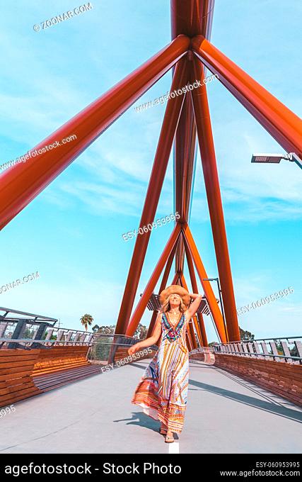 Carefree smiling woman walking vicaciously across a modern foot bridge across the river