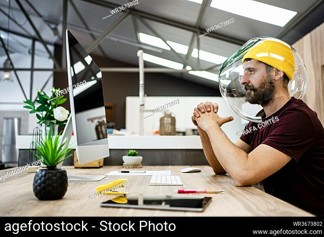 Businessman wearing fishbowl while using computer in modern office