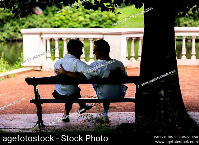 PRODUCTION - 03 July 2021, Lower Saxony, Oldenburg: ILLUSTRATION - Two men sit together arm in arm on a park bench. (posed scene) Photo: Mohssen...