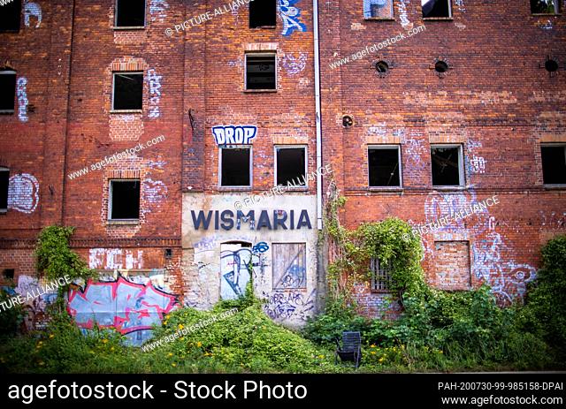 28 July 2020, Mecklenburg-Western Pomerania, Wismar: The 130 year old empty and partially collapsed malt factory stands on the Mühlenteich pond right next to...