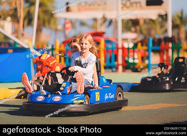 Young girls riding in electric toy car in a coastal region on a sunny day