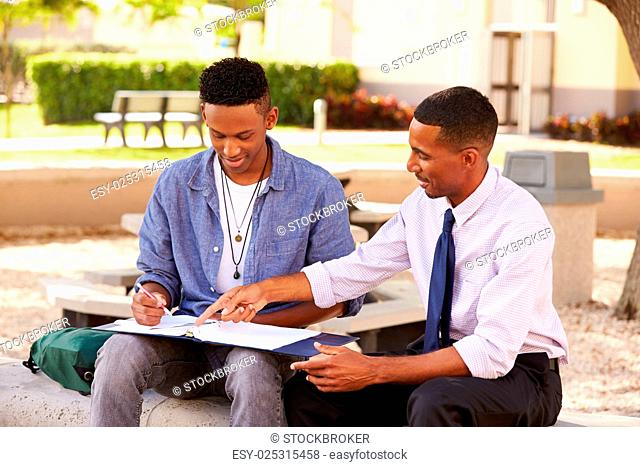 Teacher Sitting Outdoors Helping Male Student With Work