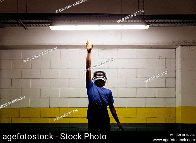 Young man wearing astronaut helmet reaching LED light with hand raised at subway