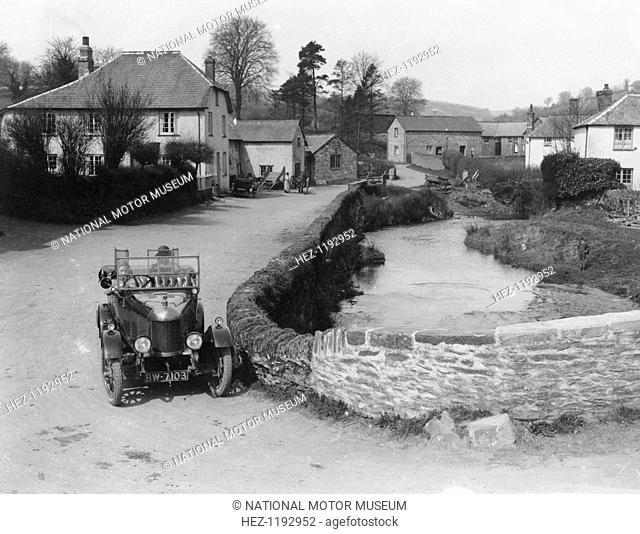 1923 Morris Bullnose at Exford in Somerset, (1920s?). The car is being driven by a woman alongside a stream in a quiet village