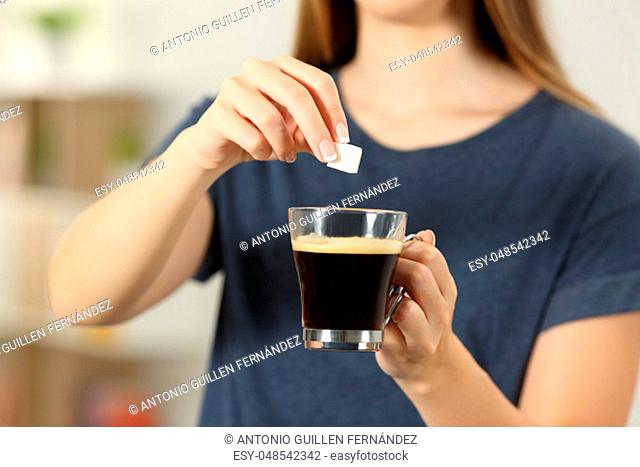 Front view close up of a woman hands throwing a sugar cube into a coffee cup at home