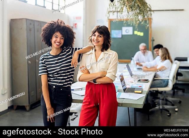 Smiling businesswoman with arms crossed by colleague in office