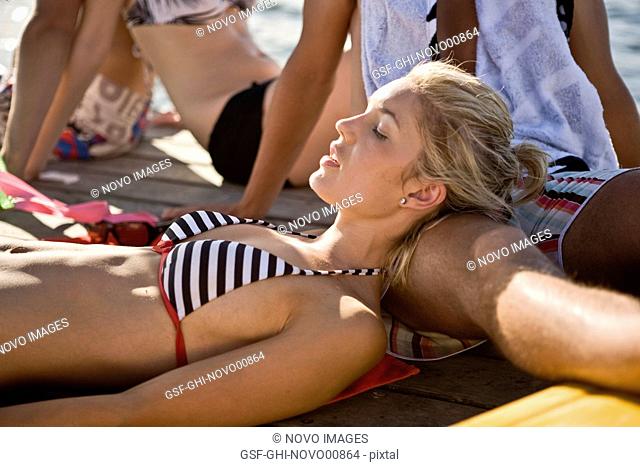Two Young Couples Sitting and Sunbathing on Edge of Pier, Close-Up of Young Blonde Woman