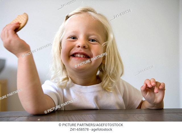 Blond little girl is is eating a coockie