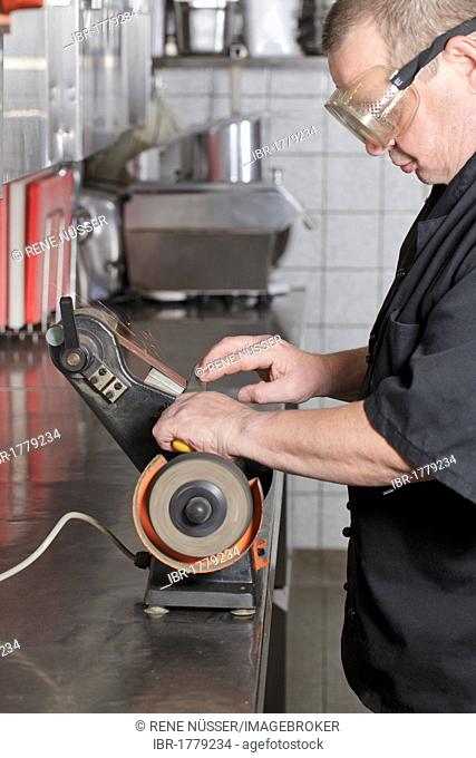Chef sharpening a knife with a belt grinder in a kitchen