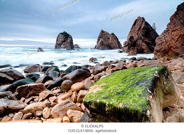 Ocean waves crashing on stones of Praia da Ursa beach surrounded by cliffs Cabo da Roca, Colares, Sintra, Portugal, Europe