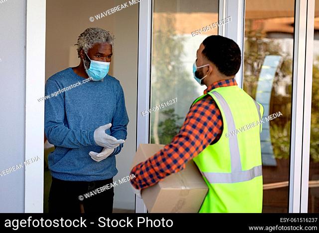 Delivery man delivering package to senior man wearing face mask at home