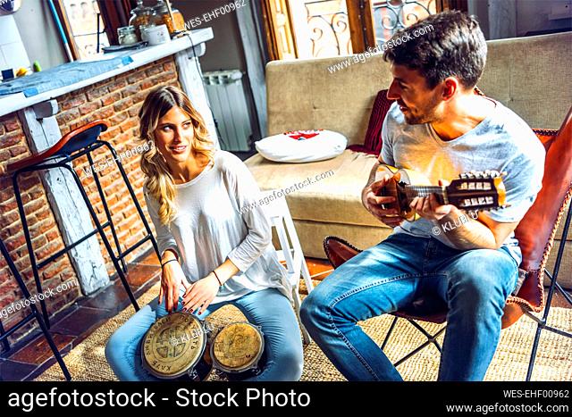 Young couple playing duet with drums and guitar in living room at home