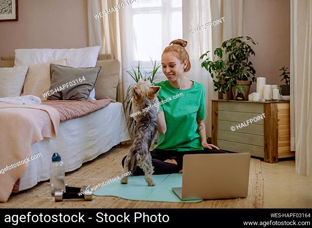 Smiling woman stroking pet dog on exercise mat at home