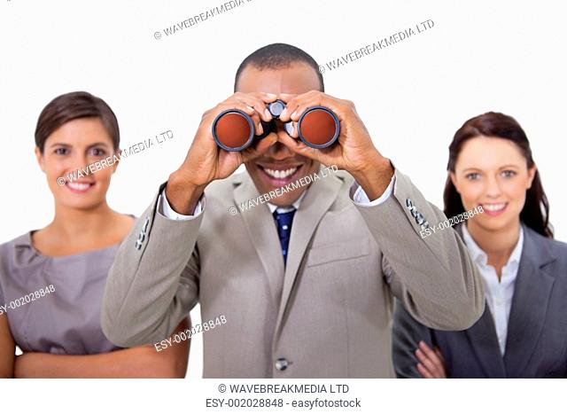 Smiling businessman with colleagues looking through binoculars against a white background