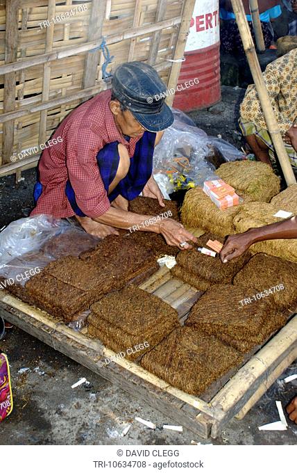 Middle aged man sitting in market selling blocks of hand rolling tobacco Aikmel Lombok Timur NTB Indonesia