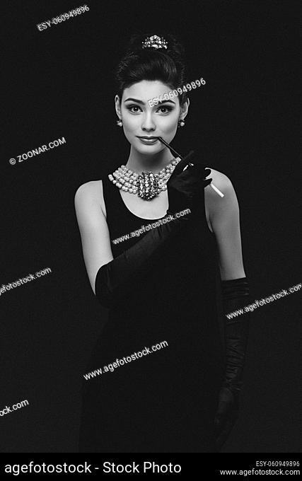 Beautiful woman looking like Audrey Hepburn standing with cigarette-holder
