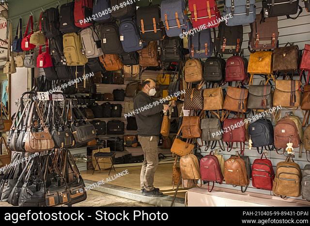 05 April 2021, Greece, Athen: The shopkeeper wears a mouth-to-nose covering as he arranges the bags in his shop. From Monday, 05.04