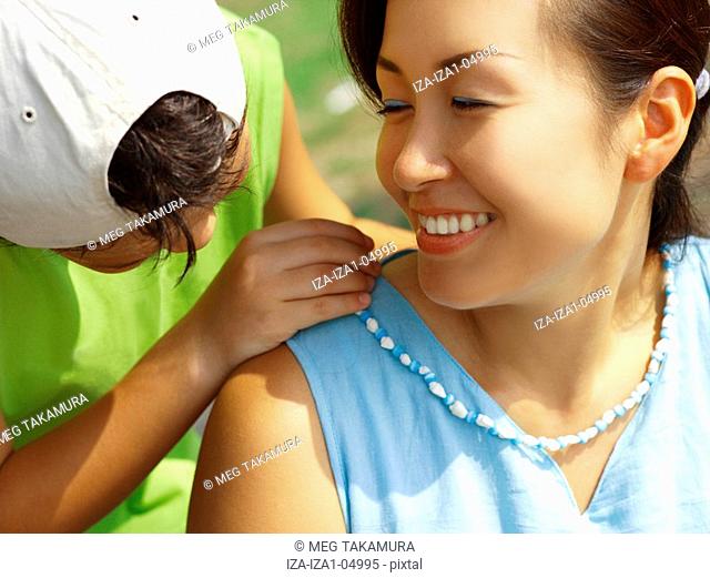 Close-up of a boy putting a necklace around his mother's neck