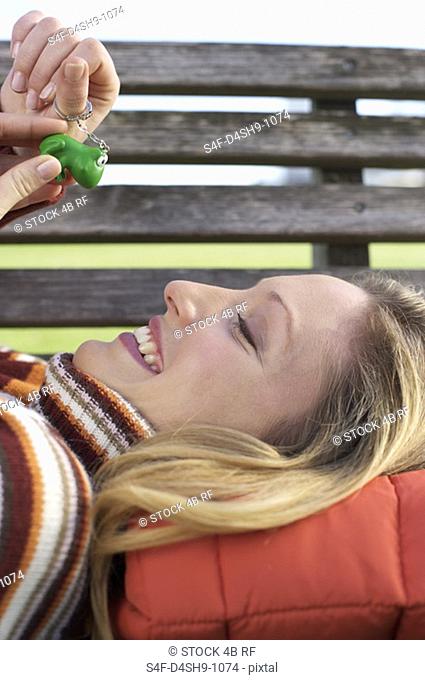 Young woman lying on a wooden bench with a key ring pendant in her hand, close-up